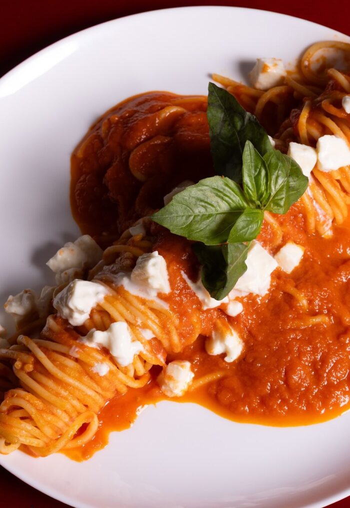 Este prato clássico apresenta spaghettoni, uma massa de espessura mais grossa que o espaguete tradicional, envolta em um vibrante molho pomodoro. O molho tem uma consistência cremosa e encorpora um tom vermelho-alaranjado, sugerindo a presença de um ingrediente cremoso, como creme de leite ou queijo.